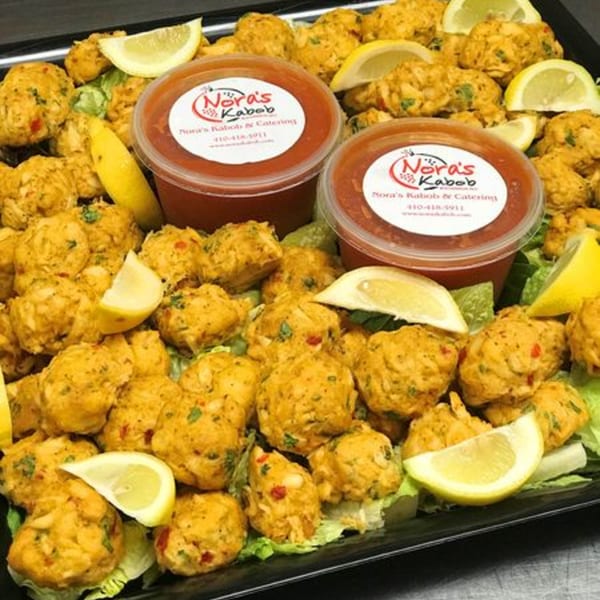 Noras Kabob's golden-brown falafel, garnished with lemon wedges and two containers of red sauce.