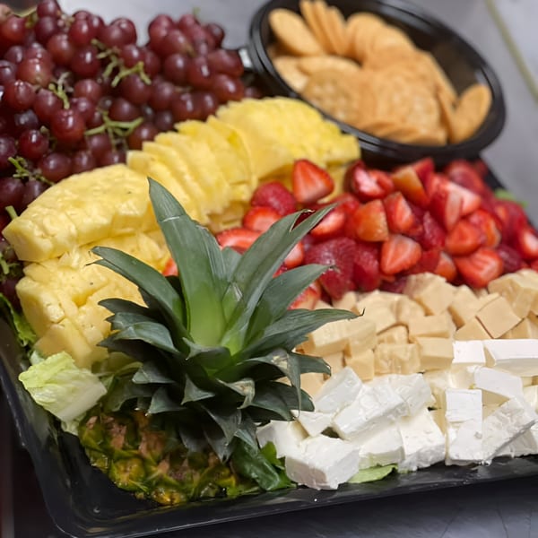 A Noras Kabob platter with red grapes, pineapple, strawberries, cheese cubes, and crackers.