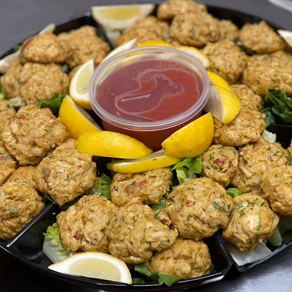 A platter of golden-brown crab cakes with lemon wedges, lettuce, and a cup of red sauce.