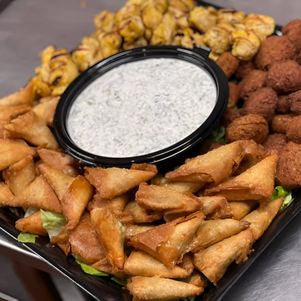 A platter of golden-brown fried pastries, falafel, and chicken, with a white dipping sauce.