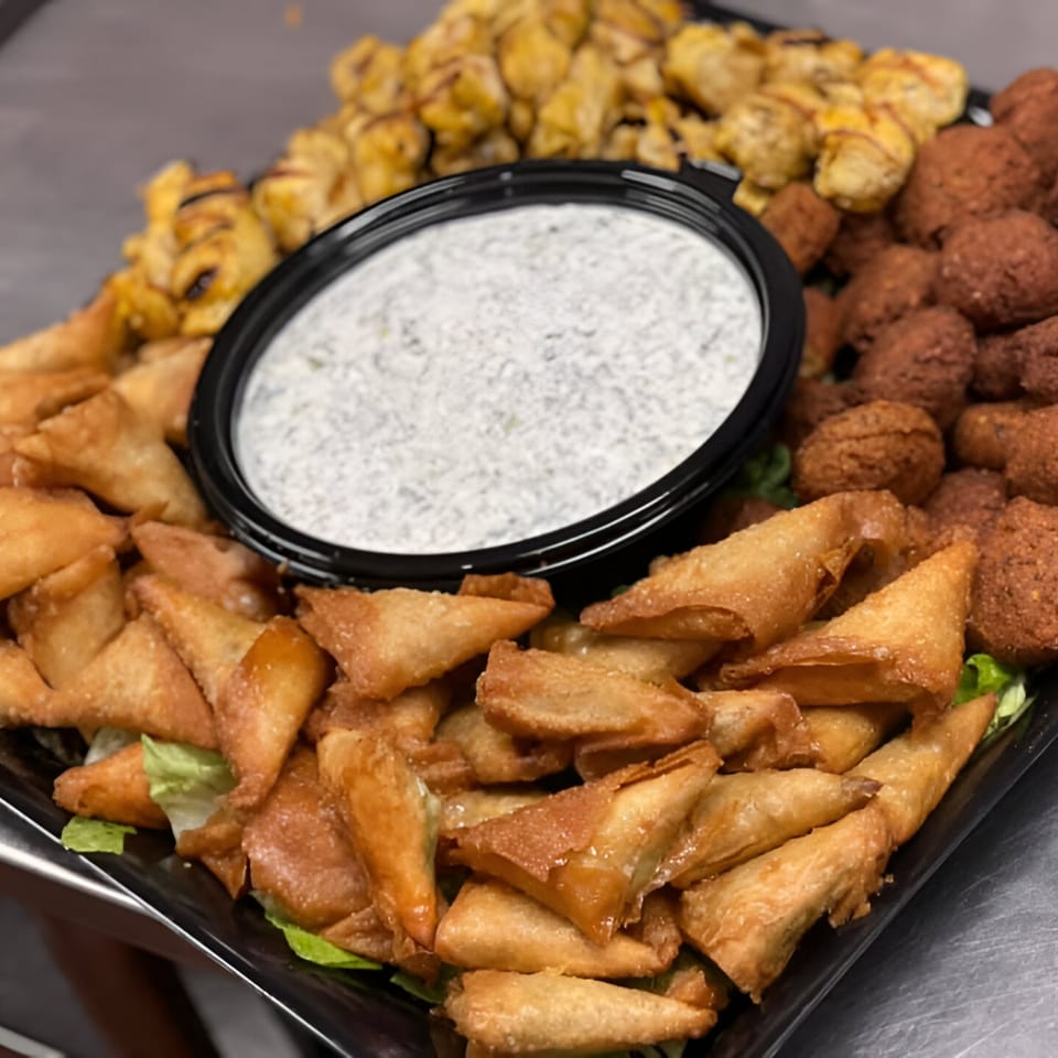 A platter of golden-brown fried pastries, falafel, and chicken, with a white dipping sauce.
