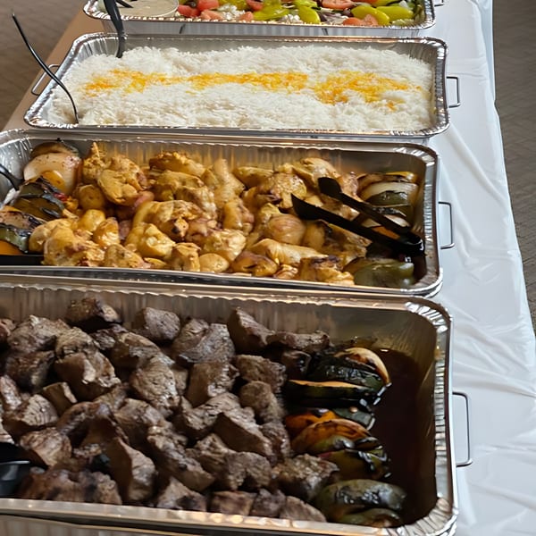 Buffet of Mediterranean food including rice, chicken kabobs, beef kabobs, and grilled vegetables.