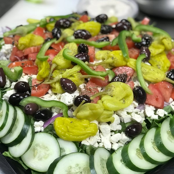 A vibrant Mediterranean salad with cucumbers, tomatoes, feta, olives, and peppers from Noras Kabob.