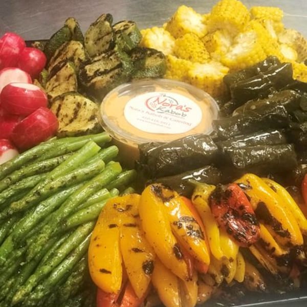 A platter of grilled vegetables, including zucchini, corn, bell peppers, asparagus, radishes, and stuffed grape leaves.