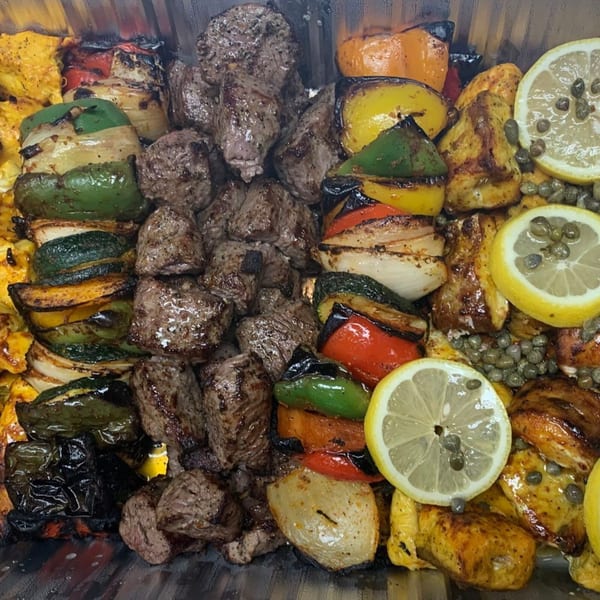 Grilled beef and chicken kabobs with colorful vegetables, lemons, and capers from Noras Kabob.