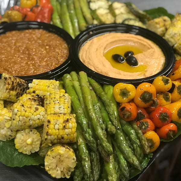 Mediterranean platter with hummus, red pepper dip, grilled corn, asparagus, and mini bell peppers.
