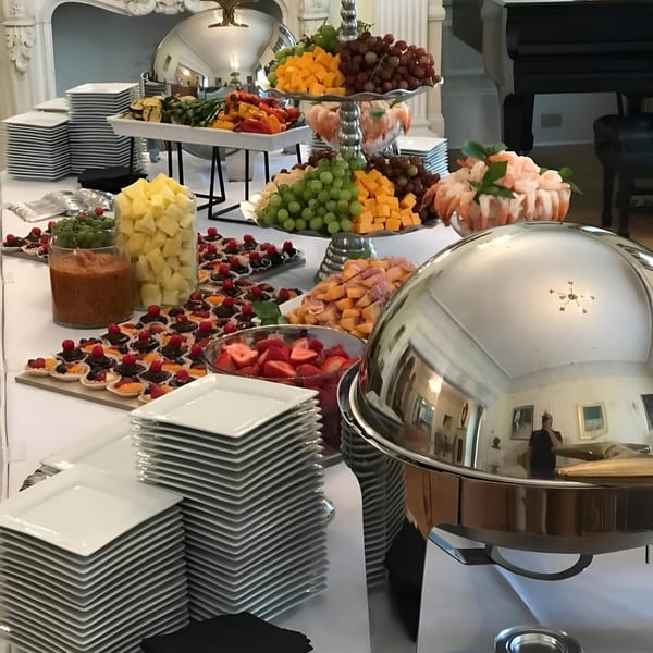 A buffet table laden with Mediterranean appetizers, fruits, desserts, and chafing dishes in an elegant room.