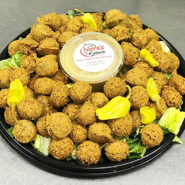 A platter of golden-brown falafel balls, lettuce, yellow peppers, and a Nora's Kabob sauce cup.