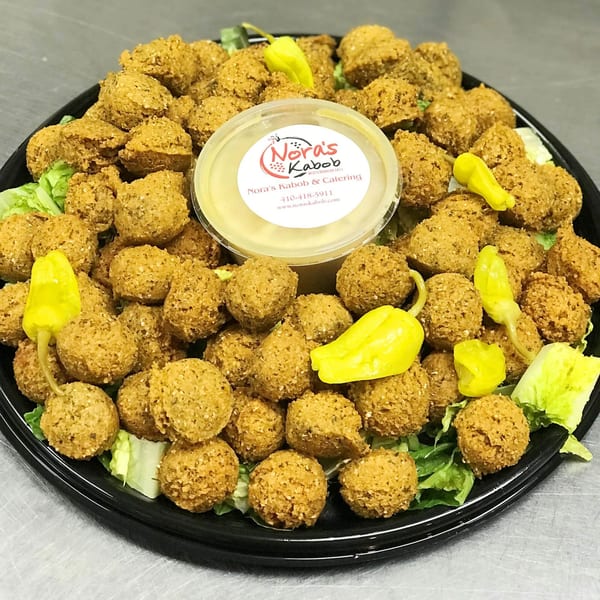 A platter of Nora's Kabob falafel with lettuce, yellow peppers, and a side of sauce.