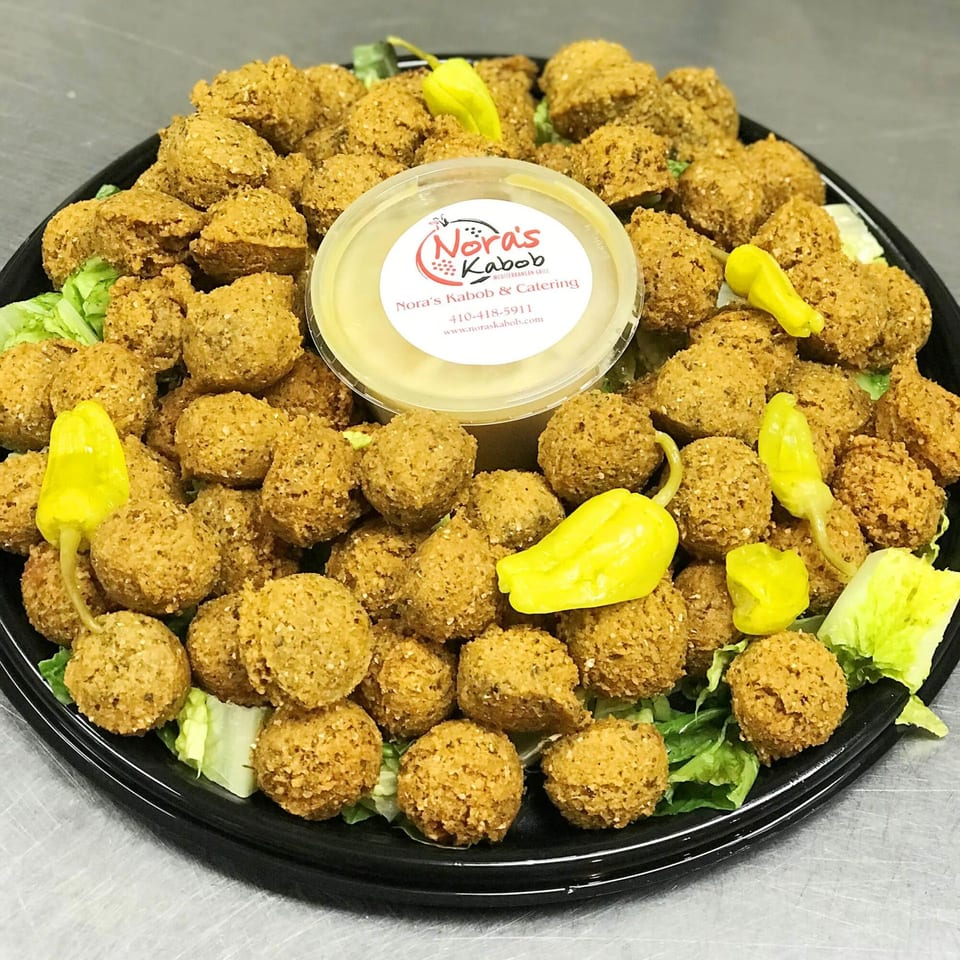 A platter of Nora's Kabob falafel with lettuce, yellow peppers, and a side of sauce.